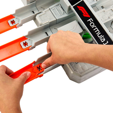 Hands connecting orange track pieces to the gray Formula 1 three-lane booster