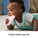 Baby chewing on the pink gua sha teether during tummy time