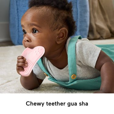 Baby chewing on the pink gua sha teether during tummy time