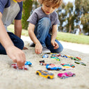 Two boys playing with Hot Wheels cars on a sandy path outdoors