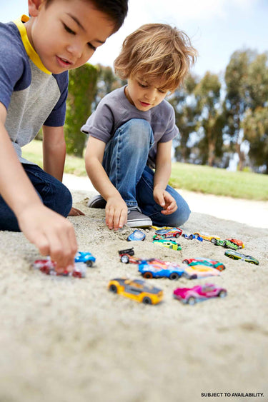 Two boys playing with Hot Wheels cars on a sandy path outdoors