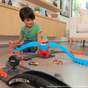 Child playing with connected Hot Wheels City sets and cars on a living room floor