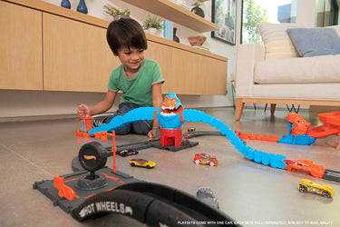 Child playing with connected Hot Wheels City sets and cars on a living room floor