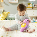 Baby sitting on a rug squeezing the pink Fisher-Price Soothe & Glow Seahorse
