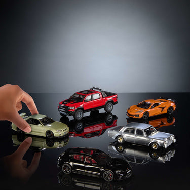Hand placing a Hot Wheels Premium 1:43 car among several other 1:43 scale cars on a dark surface
